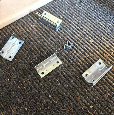 four brackets on a carpet, with screws and a piece of wood nearby.