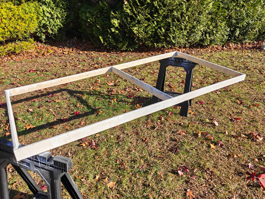 paint drying one wooden flat, propped up by a couple of sawhorses in a grassy yard. It has a coat of white paint, which is drying.