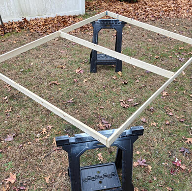 a frame, before painting one wooden flat, propped up by a couple of sawhorses in a grassy yard. It is awaiting paint.
