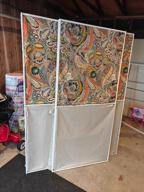 two wooden frames, standing, with paisley cloth stretched across the top half of each and beige cloth stretched across the bottom half of each.